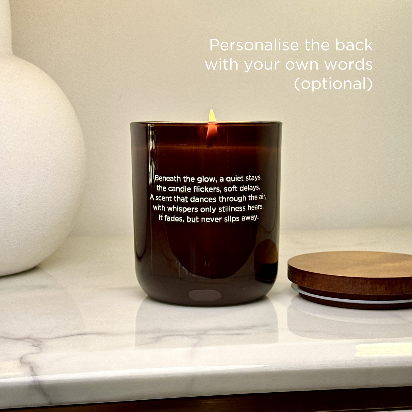 The back of a Lakewood Candles Cinnamon + Spice candle with optional custom text. The image showcases a burning candle with poetic text that captures a slow, romantic mood. Customers can personalise this area with their own message, making each candle unique. Perfect for gifting or commemorating special moments. Set on a marble bench with neutral decor. Aesthetic, calm, and heartfelt.