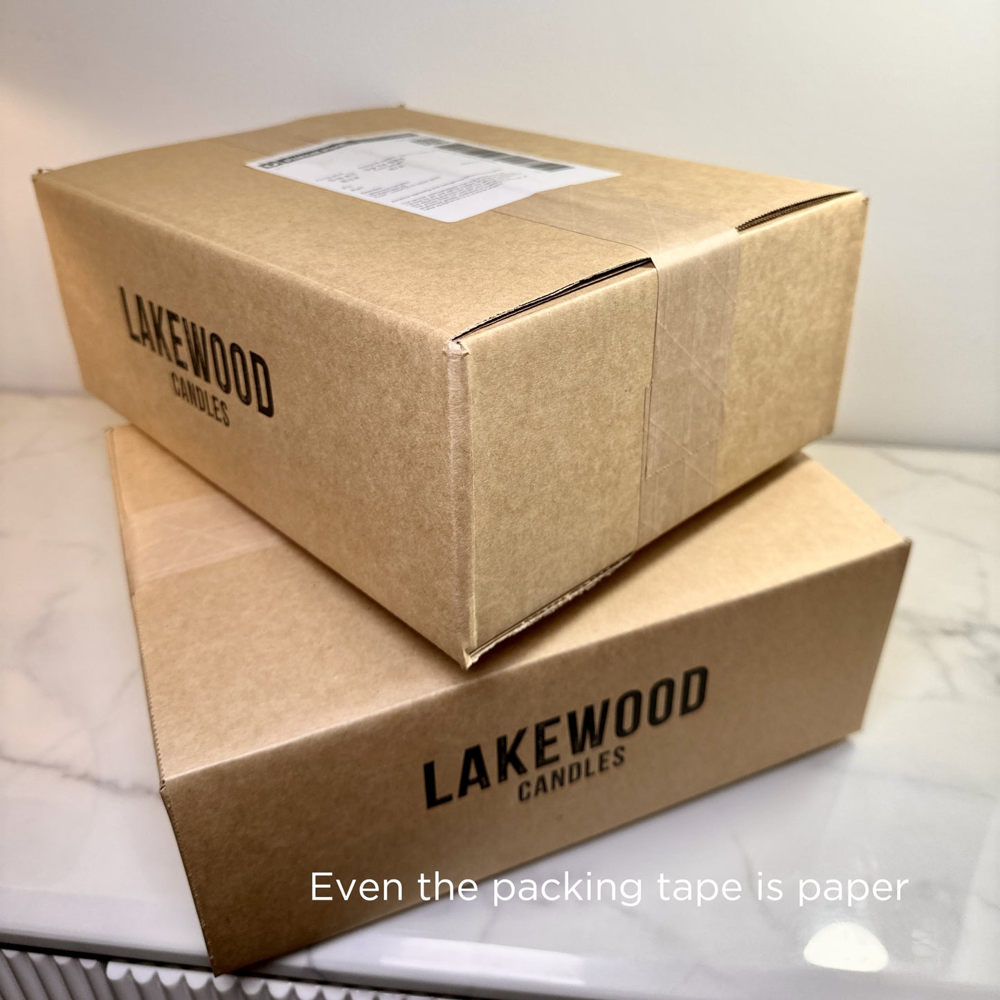 Two Lakewood Candles shipping boxes stacked, fully sealed with recyclable paper tape—no plastic. The image reinforces the brand’s commitment to sustainability from product to packaging. Set on a marble bench, the minimalist aesthetic aligns with eco-conscious values. Perfect for promoting ethical, plastic-free shipping practices in eCommerce and handmade goods.