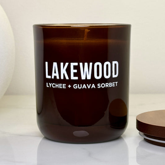 Close-up of burning Lakewood candle in amber glass jar with white text “Lychee + Guava Sorbet.” Presented without lid on a stone benchtop, highlighting the warm tone of the wax and soft ambient flame. Ideal gift for birthdays, celebrations or self-care moments. Designed for scent lovers who appreciate elegant, eco-conscious home fragrances made in Australia.