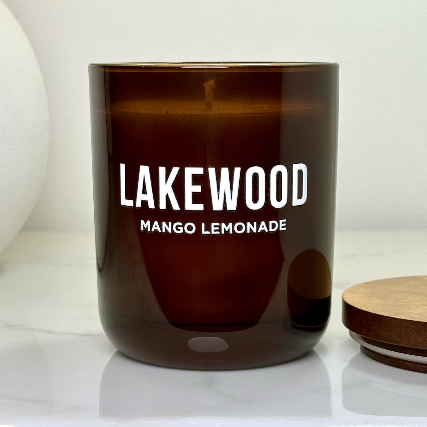 Open Mango Lemonade Lakewood Candle with warm wax visible, lid off to the side, displayed on a clean marble bench