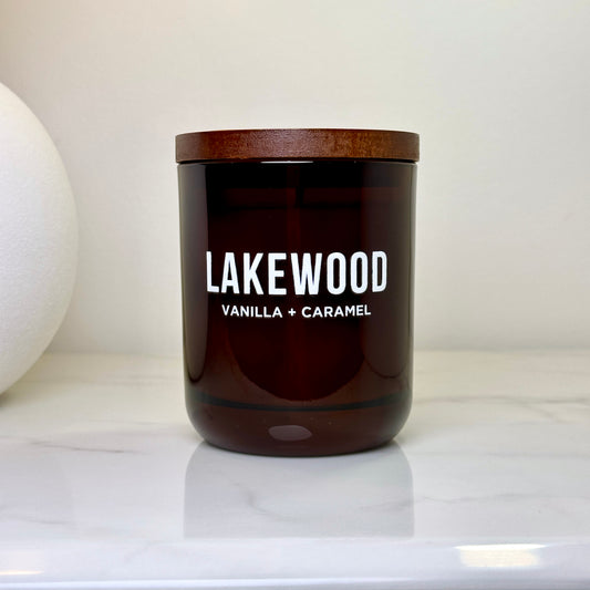LAKEWOOD Vanilla + Caramel candle in a sleek amber glass jar with a wooden lid, styled on a white marble surface. This large, natural soy wax candle delivers a warm, rich scent of creamy vanilla and buttery caramel. Designed for modern Australian interiors, it’s the perfect eco-luxury gift or home addition. Handmade with care, clean burning, and packaged plastic-free with paper wrap. A thoughtful scent with comforting notes and minimalist style for your home.