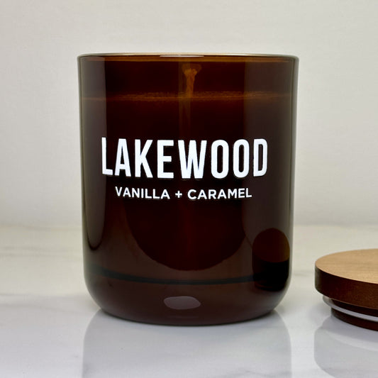 Close-up of the LAKEWOOD Vanilla + Caramel candle with the lid off, showing the smooth wax surface. This soy wax candle is handmade in Australia and infused with a warm blend of vanilla and caramel. It comes in a reusable amber glass jar with a wooden lid, delivering 48+ hours of burn time. The elegant, minimal packaging is plastic-free, with eco-conscious wrapping and paper tape. Ideal for gifting or adding a cozy, inviting scent to your living space.