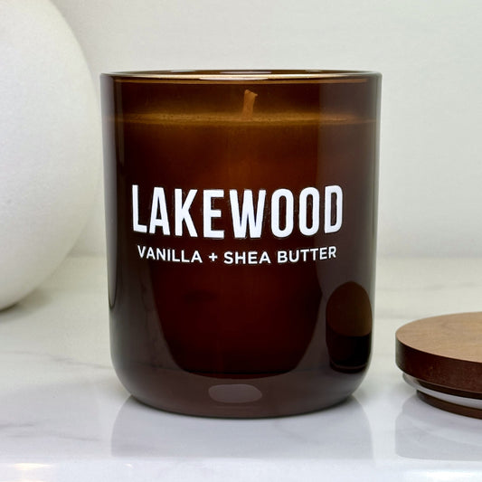 Close-up of the Vanilla + Shea Butter Lakewood candle with lid off, showing the smooth wax and wick inside the amber glass vessel on a marble surface.