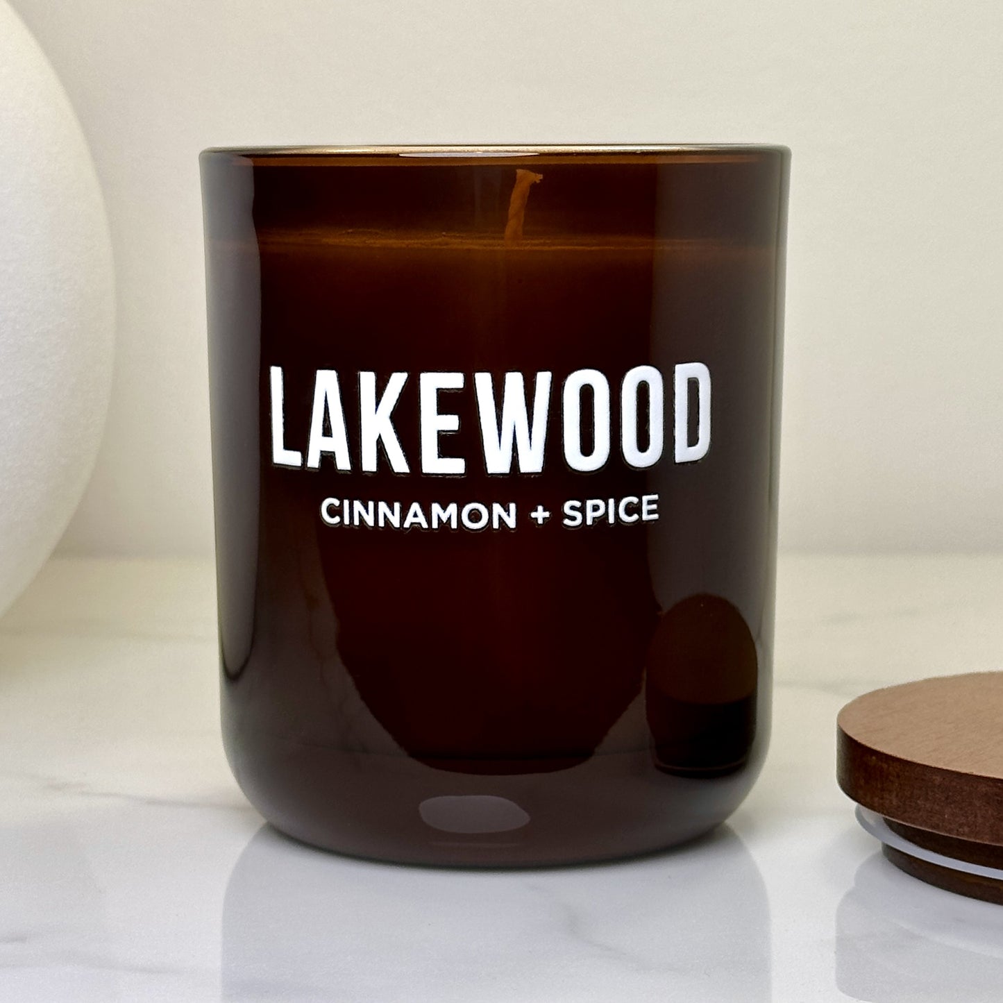 Lakewood Candles’ Cinnamon + Spice soy wax candle in an amber glass jar with white lettering and no lid. The candle is lit, creating a warm and cozy glow. Set on a marble surface with a minimalist background, this image highlights the inviting atmosphere and premium craftsmanship of the handmade candle. A perfect home scent for fans of rich, spicy, nostalgic aromas. Eco-friendly, giftable, and Australian-made.